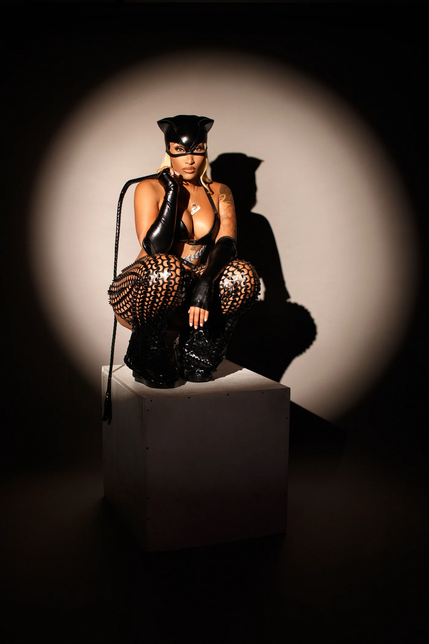 A woman in a black cat mask and costume poses on a pedestal in a circular spotlight.